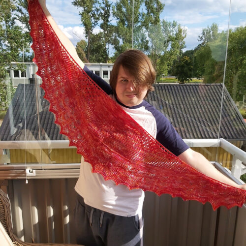 En ung man håller upp en stickad sjal