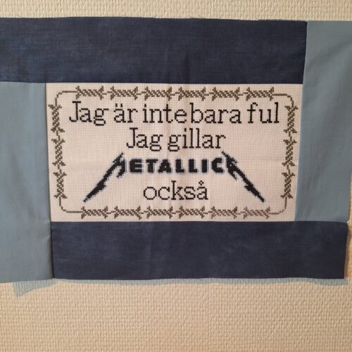 Ett korsstygn med texten "Jag är inte bara ful, jag gillar Metallica också".