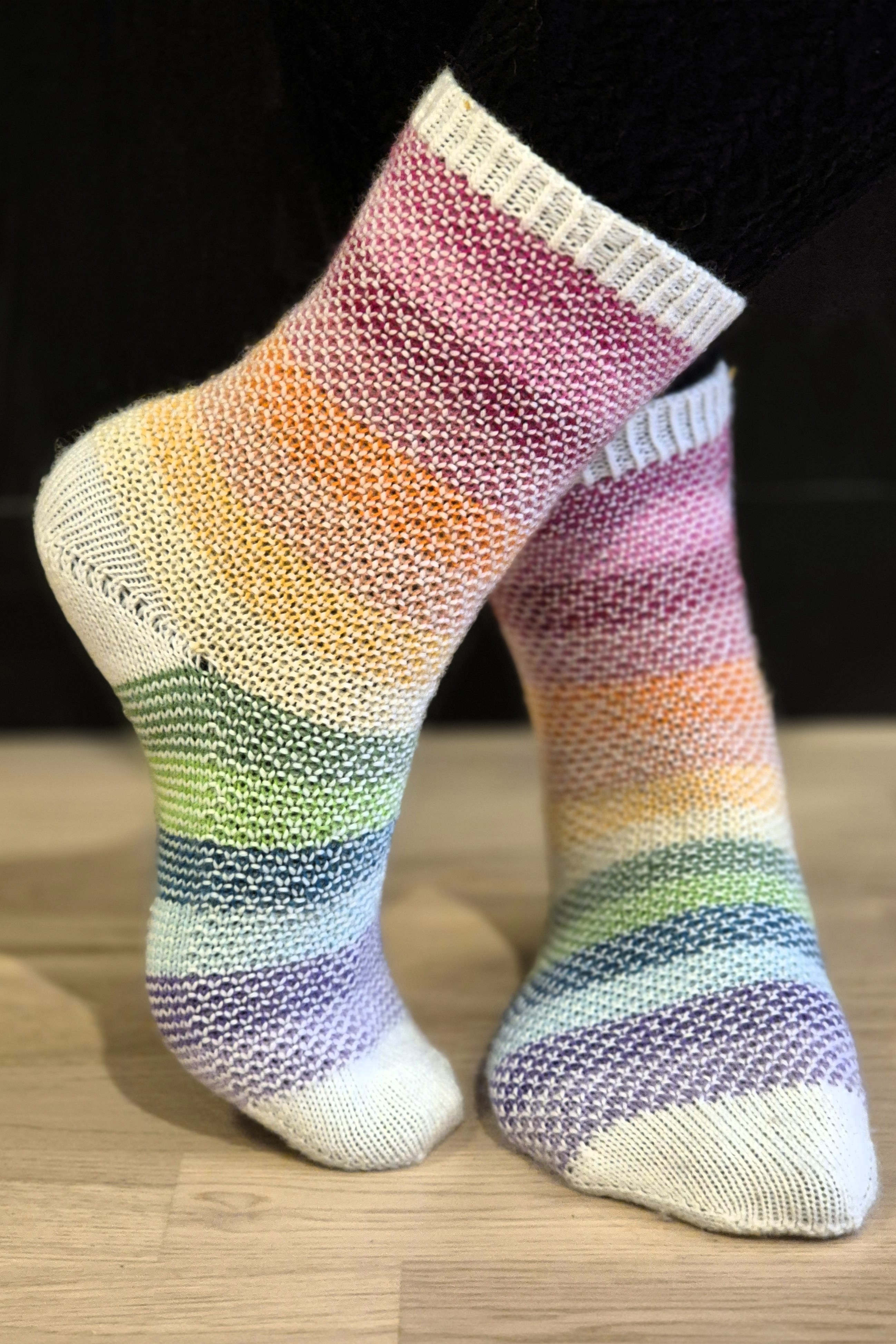Färgglada regnbågsrandiga sockar i bruten mosstickning.